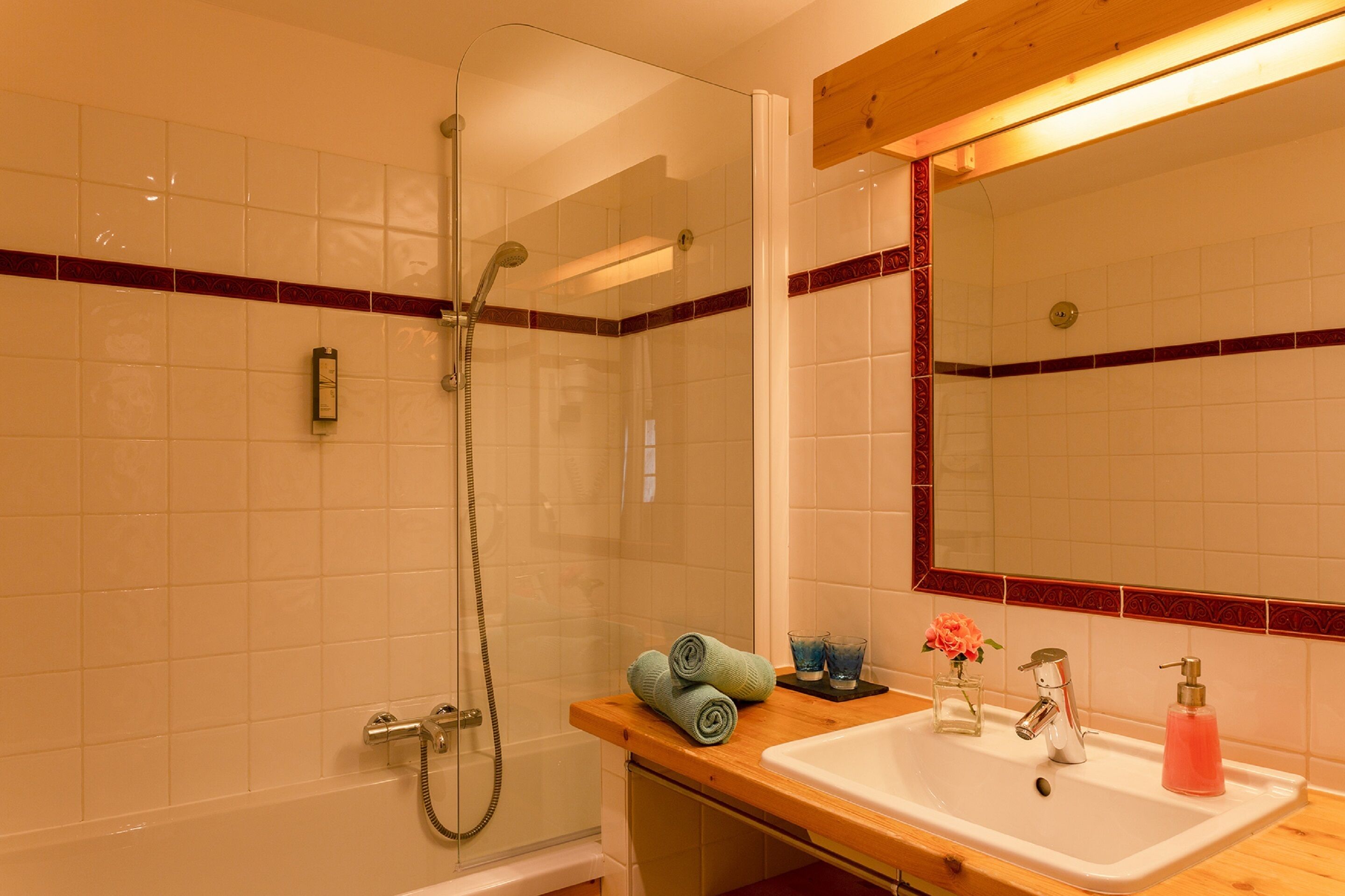 Un bagno con doccia vetro, lavandino con specchio sopra e piano in legno.