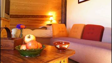 A cozy room with a wooden bed, a small table with a bowl of fruit, and a lamp.