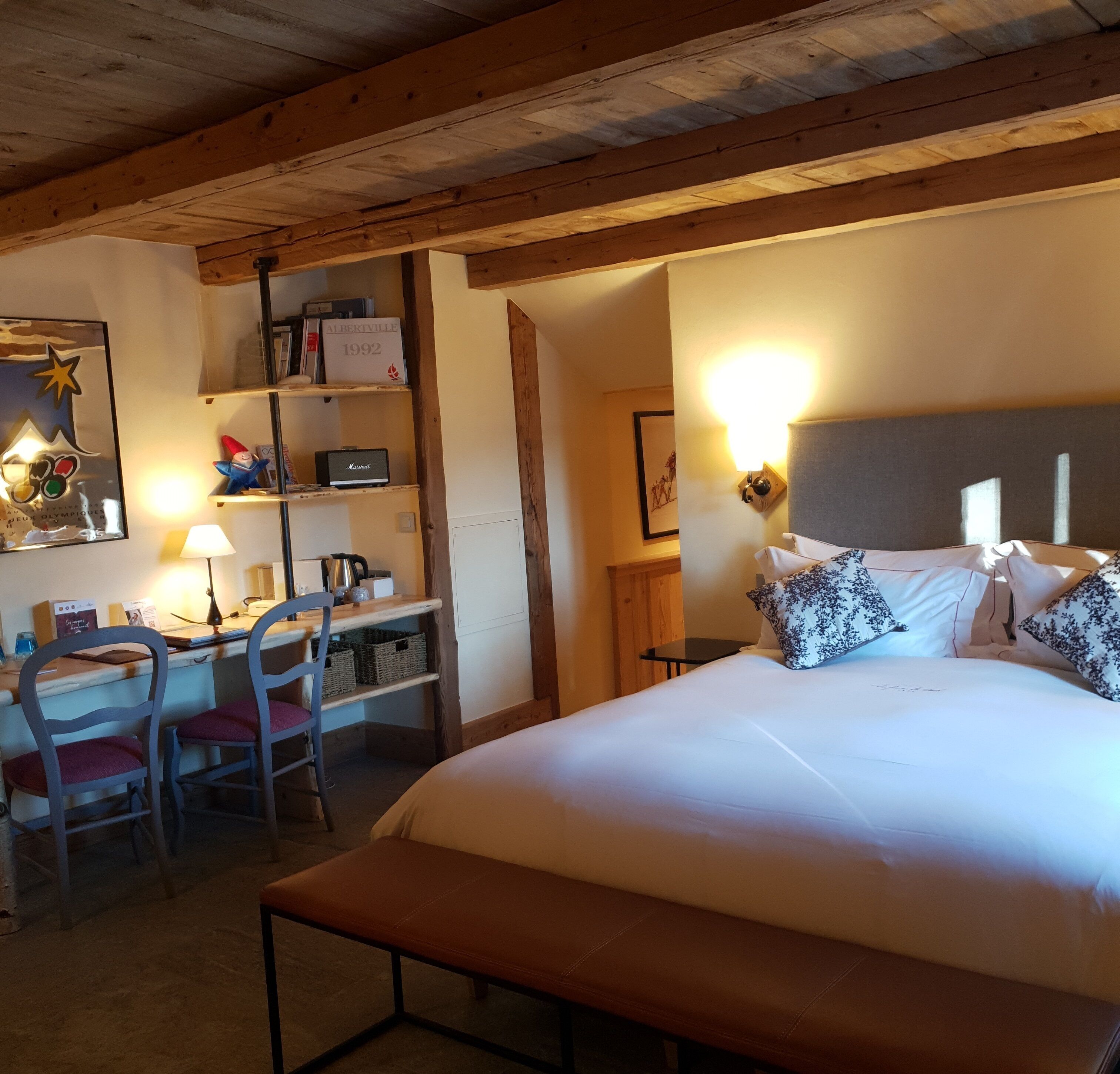Ein Schlafzimmer mit Bett, Nachttisch, Lampe, Schreibtisch mit Stuhl, Regalen und einem gerahmten Bild an der Wand.