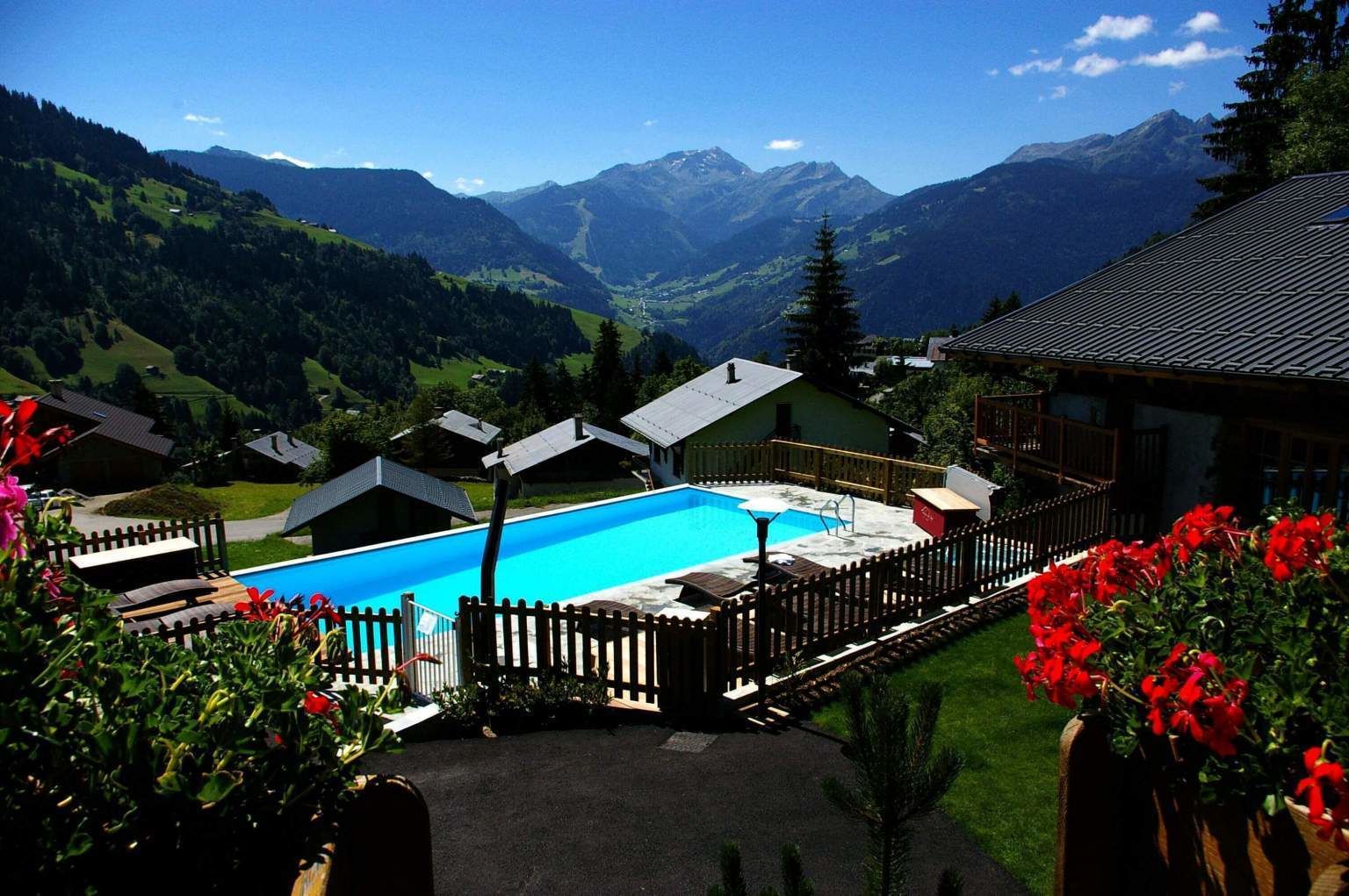 Un espace piscine offrant une vue sur les montagnes, entouré de maisons et de verdure.