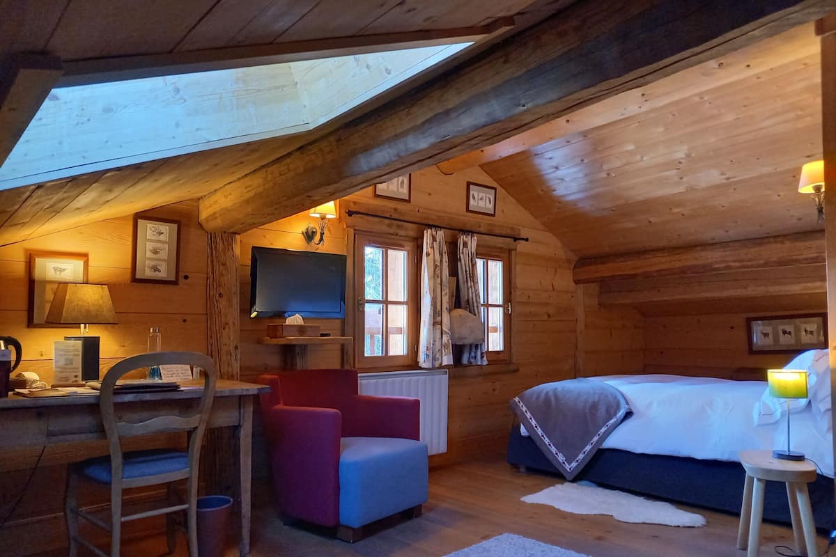 A cozy cabin room with a loft bed, a desk with a chair, a small couch, and a window with curtains.