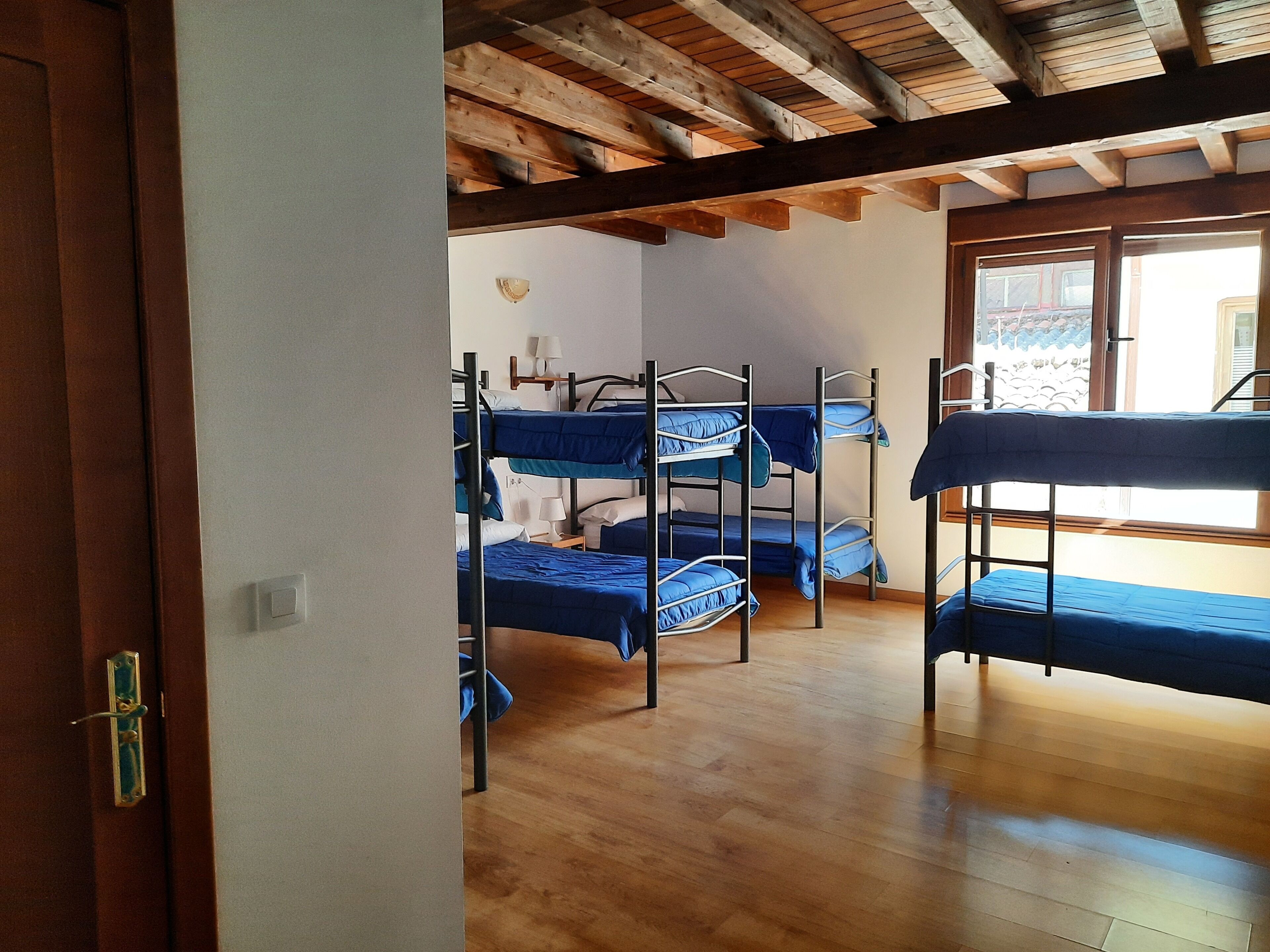A room with bunk beds, wooden flooring, and a window with a view.