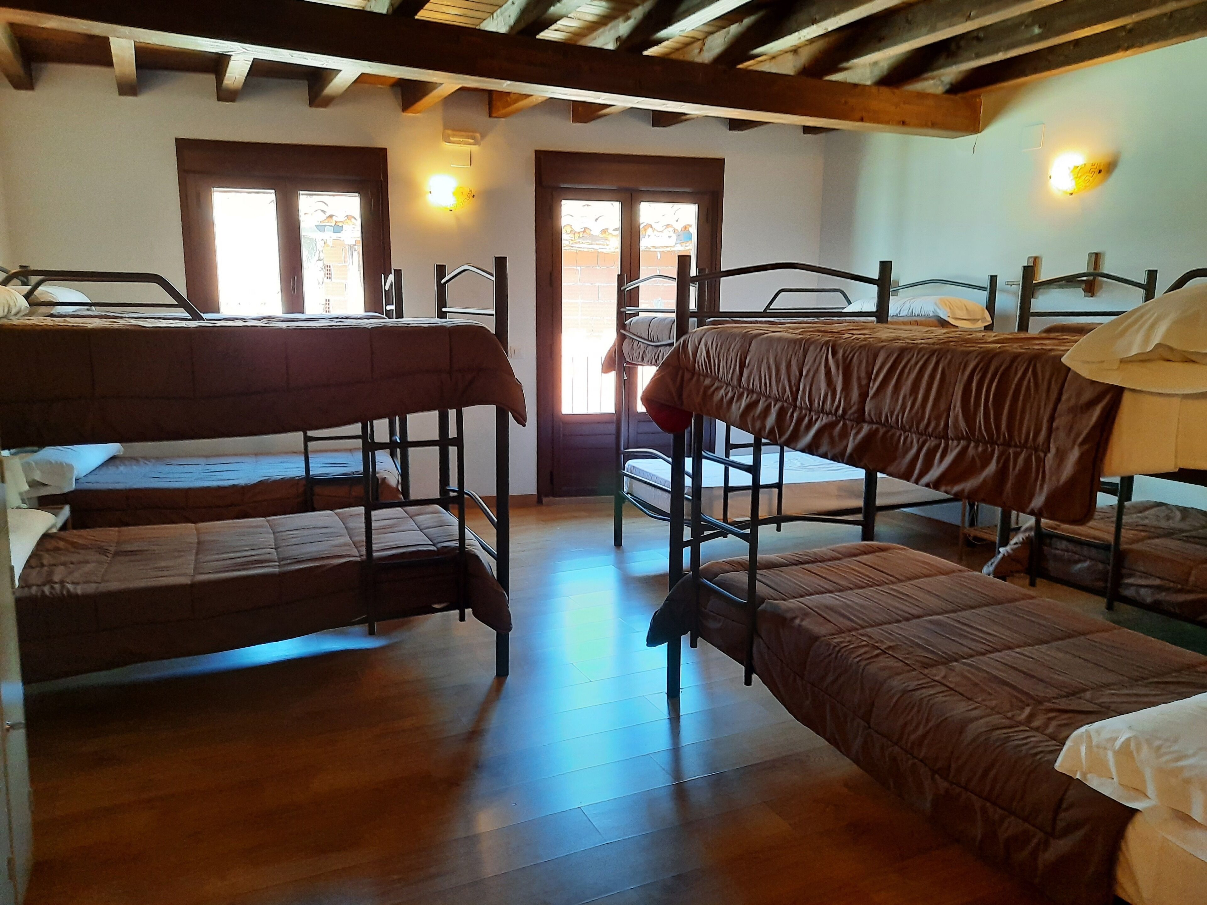 A dormitory room with bunk beds, wooden floors, and a door leading outside.