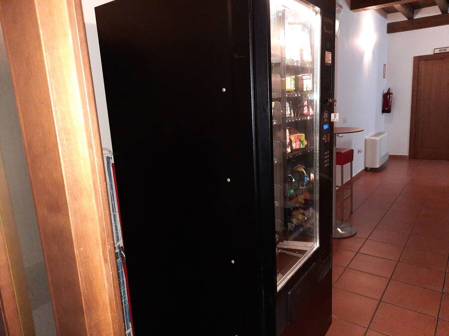 Una máquina expendedora en una habitación con suelo de baldosas y una puerta de madera.