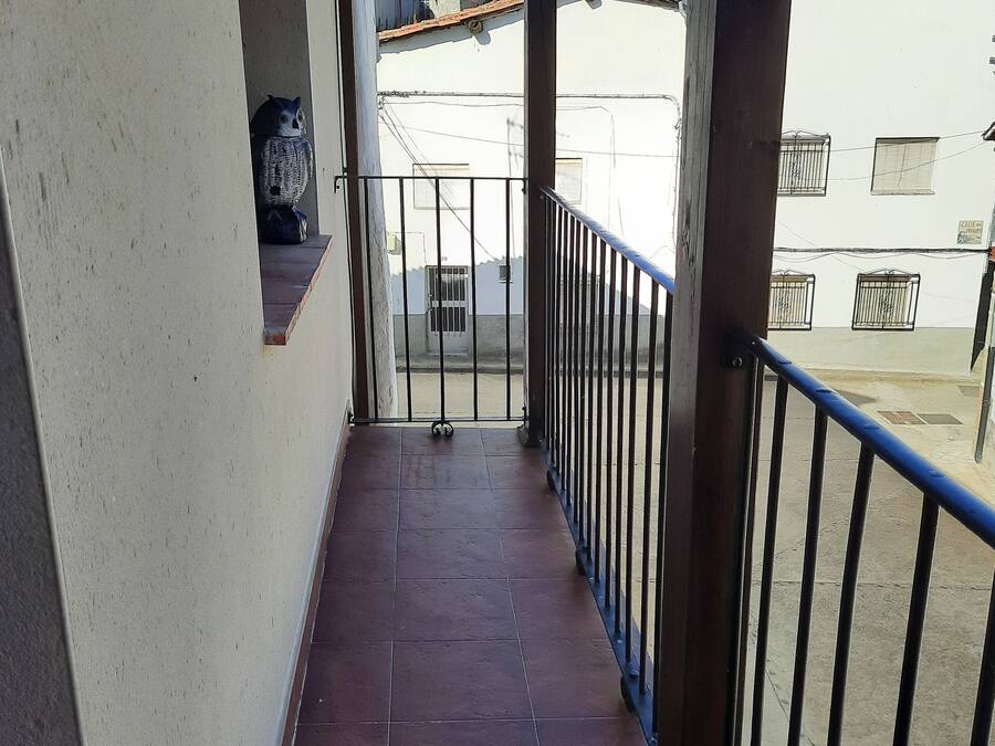 Un balcone stretto con tegole rosse, ringhiera in metallo e vista sui palazzi vicini.