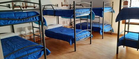A dormitory room with bunk beds, wooden floors, and wall-mounted lamps.