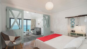 A bedroom with a bed, a chair, a nightstand, and a view of the sea through a door. - Cottage do Mar by Our Madeira (Calheta)