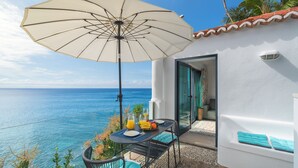 A table with a white umbrella, a glass of orange juice, and a fruit bowl on a balcony overlooking the sea. - Cottage do Mar by Our Madeira (Calheta)