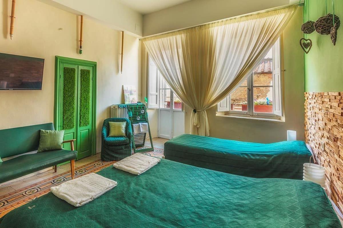 Une chambre avec deux lits, un canapé vert, une télévision et une fenêtre avec des rideaux.