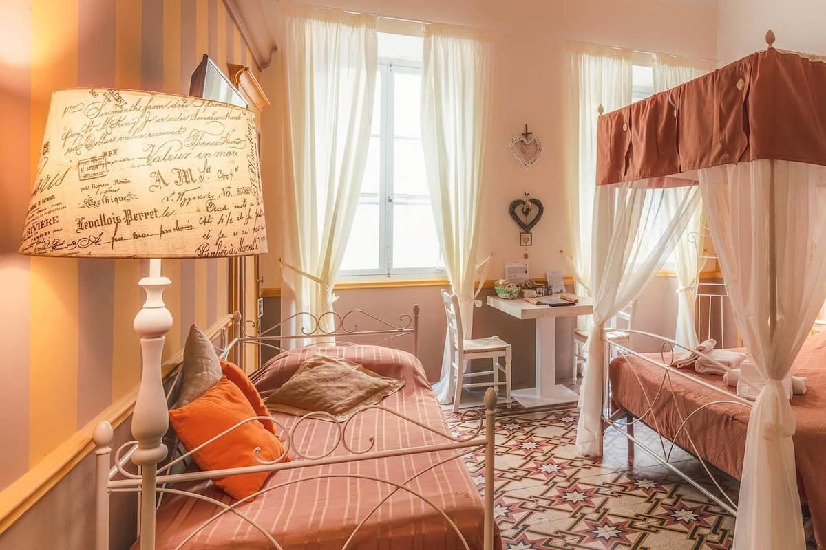 Une chambre avec deux lits, une table de chevet, une lampe et une fenêtre avec des rideaux.