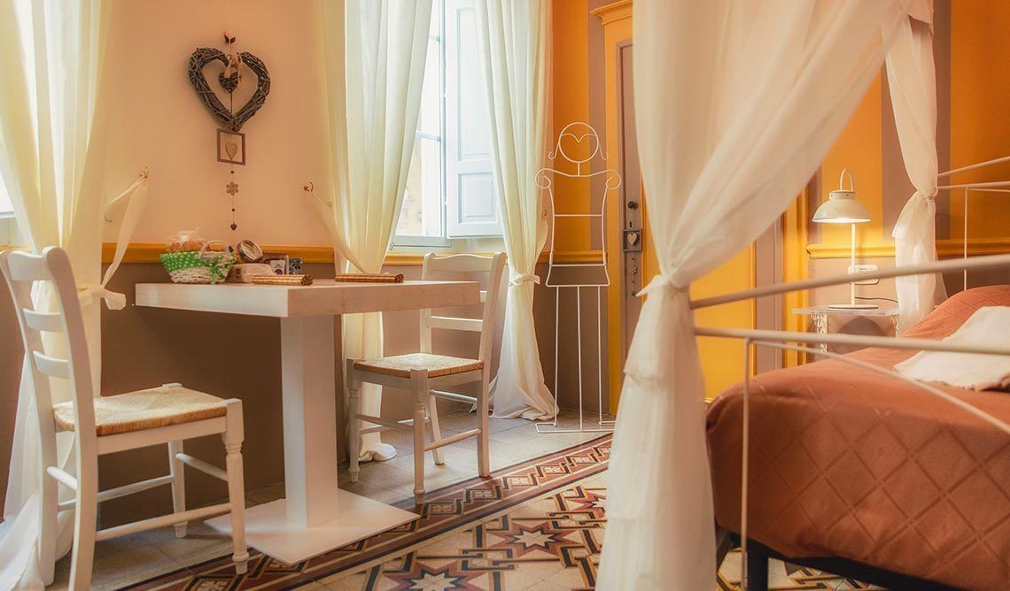 A room with a bed, a desk, chairs, and a window with curtains.