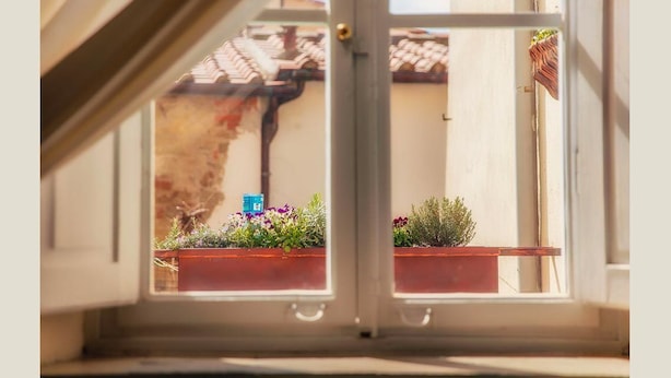 A view through a window with a view of a building's exterior, including a tiled roof and a door. - Ghibellino B&B (Arezzo)