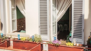 A building with two open windows, each with white shutters and a view into the interior. There are potted plants on the balcony. - Ghibellino B&B (Arezzo)