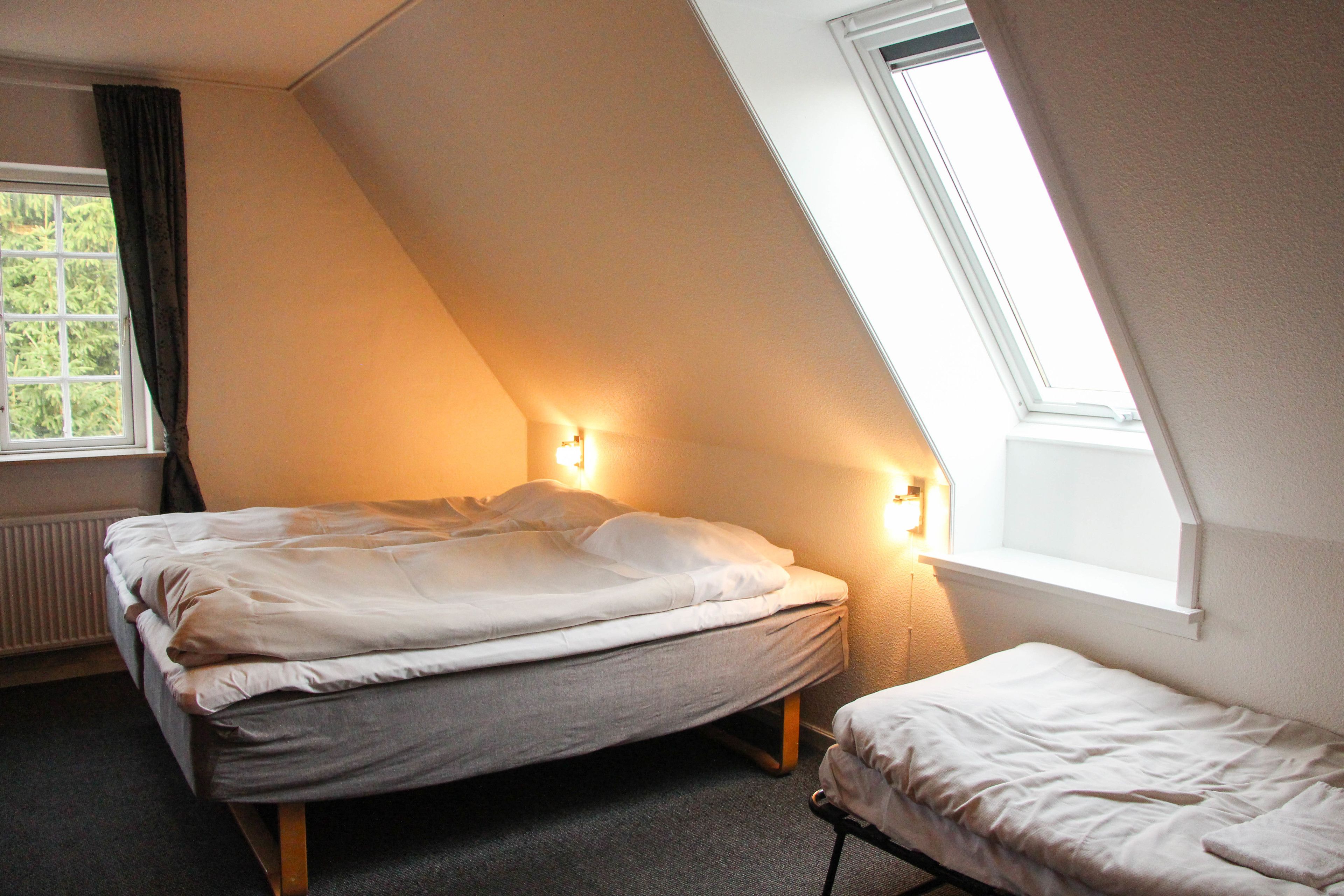 Ein Schlafzimmer mit einem Bett, einem zusätzlichen Bett oder Reisebettchen und einem Fenster mit Vorhängen.