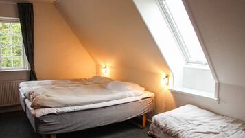 Ein Schlafzimmer mit einem Bett, einem zusätzlichen Bett oder Reisebettchen und einem Fenster mit Vorhängen.