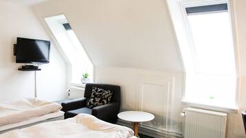 Habitación de hotel con cama, una silla, una mesita, televisor y ventana con vistas.