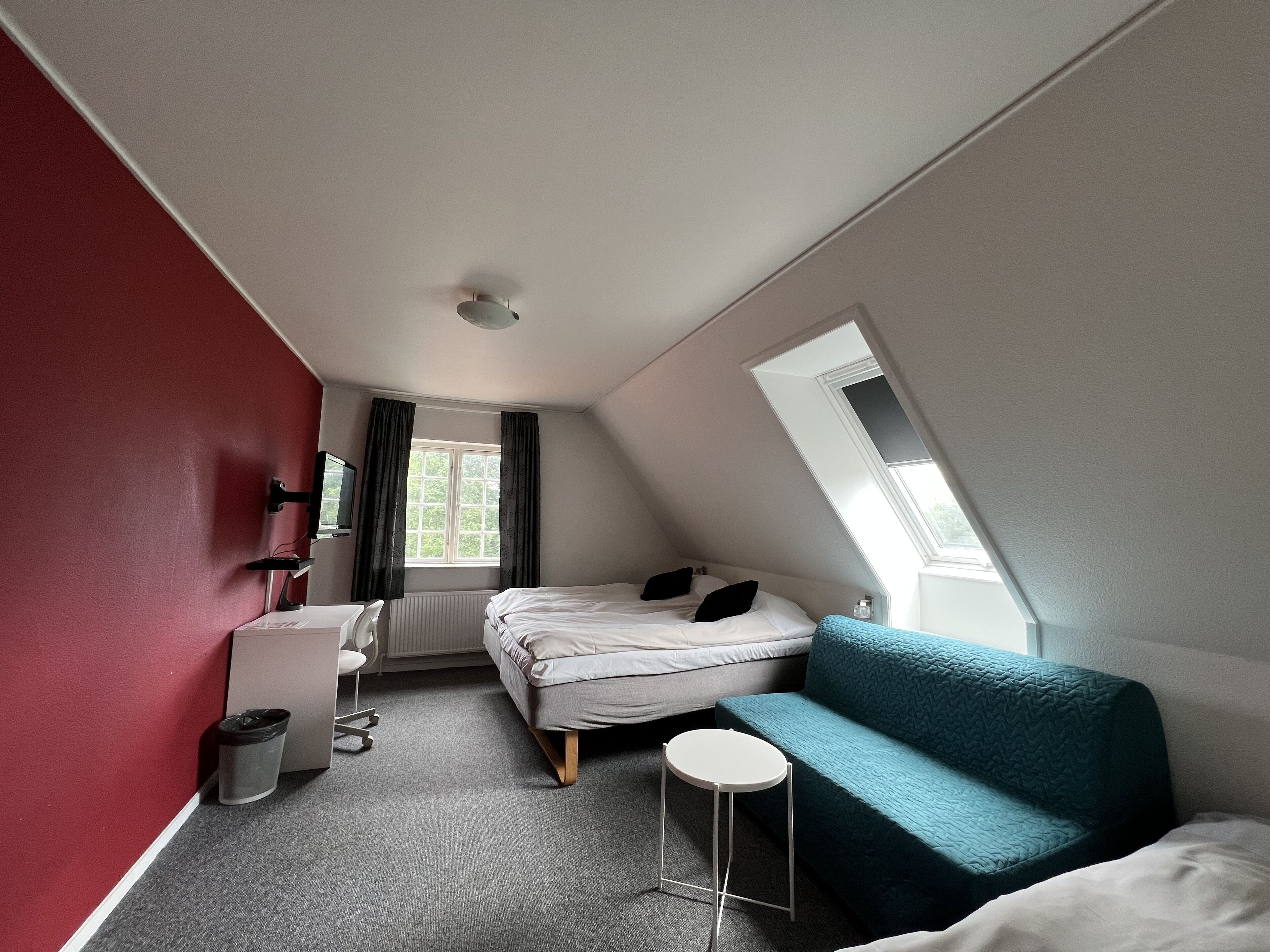 Una habitación pequeña y moderna con una cama, un sofá azul, una mesita, un escritorio y una ventana.