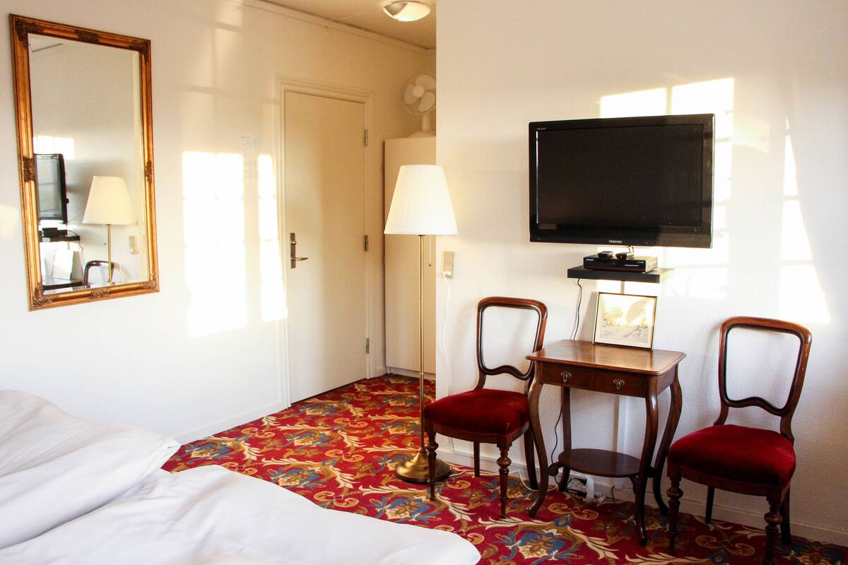 Une chambre d’hôtel comprenant un lit, un bureau avec deux chaises, une télévision et un miroir.