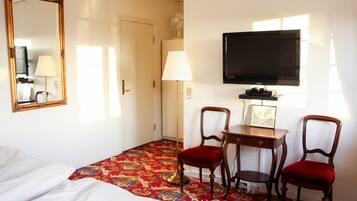 Una habitación de hotel con cama, un escritorio con dos sillas, un televisor y un espejo.