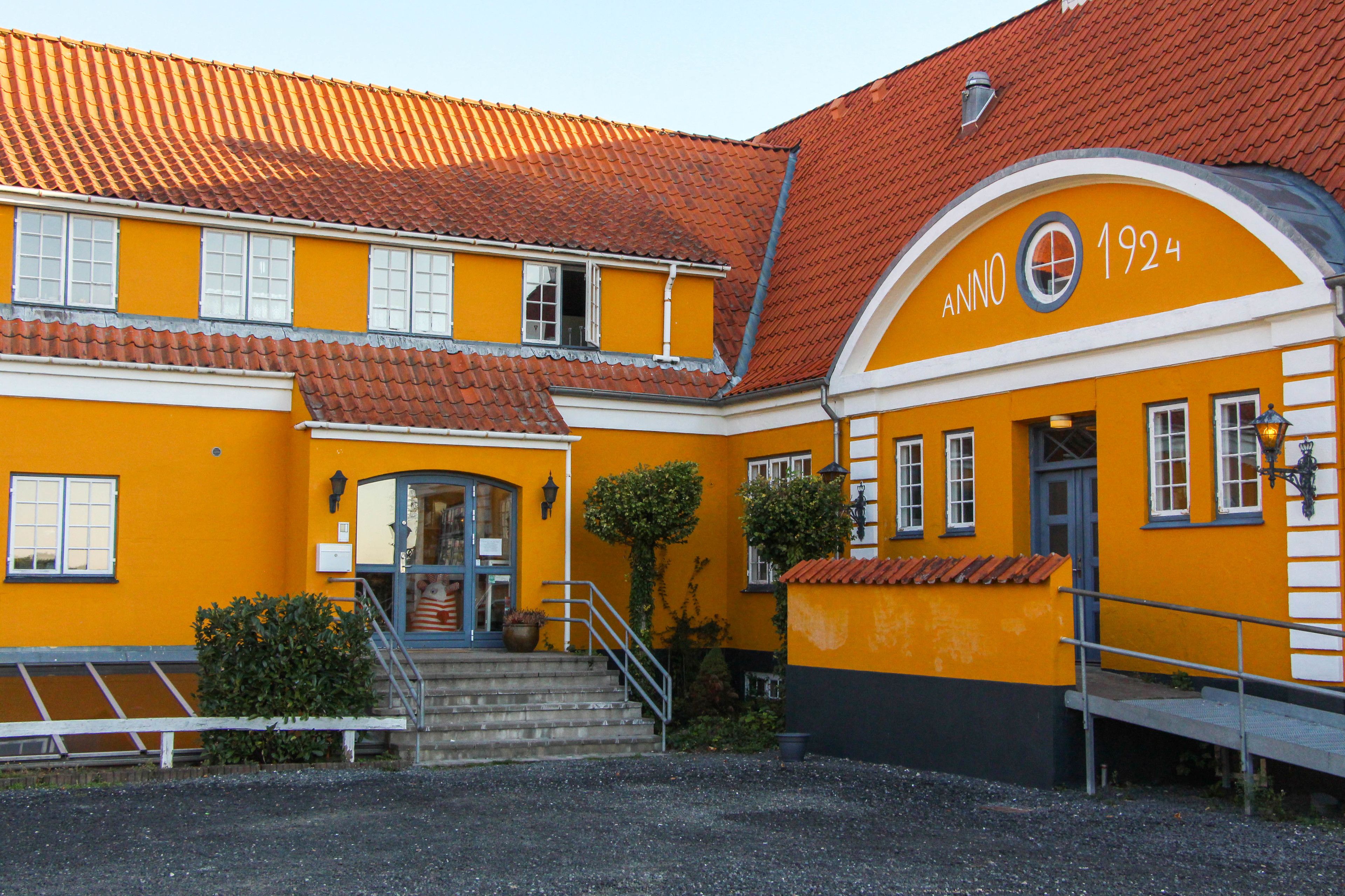 A yellow building with a red-tiled roof and a sign reading "Anno 1924".