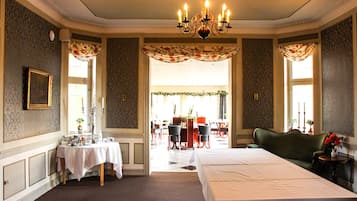 Hotellihuone, jossa on suuri sänky, kattokruunu, punaisilla tuoleilla varustettu ruokailutila ja vihreä sohva.