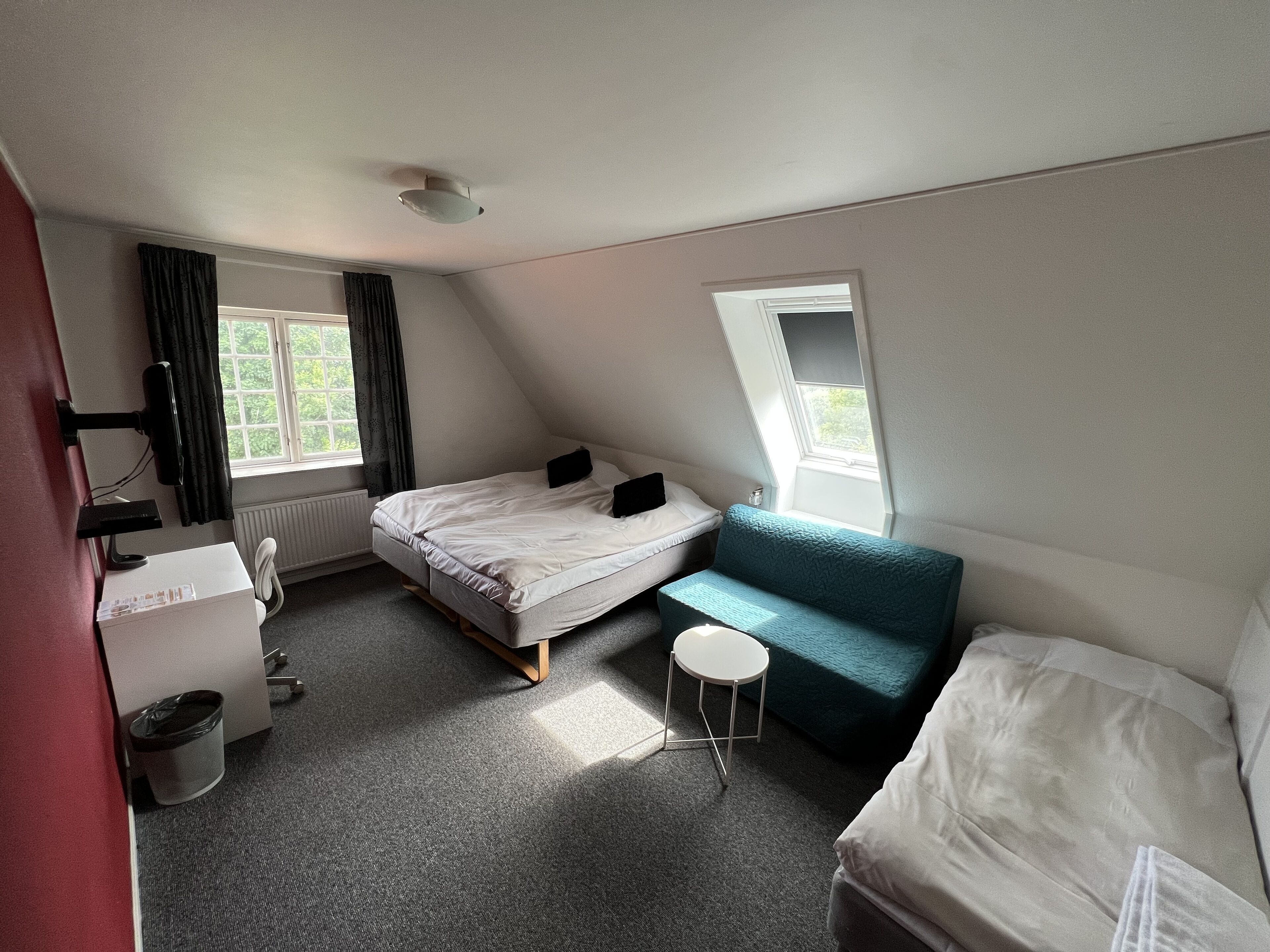 Een kleine, goed verlichte kamer met een bed, een bureau, een stoel en een raam.