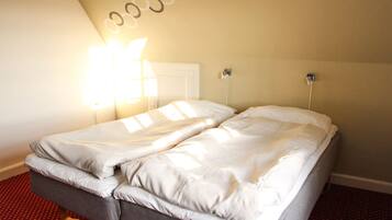 A double bed in a room with a red patterned carpet, a white door, and a wall-mounted light fixture.