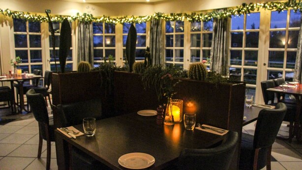 Un restaurante tenuemente iluminado con una mesa de madera oscura dispuesta para dos personas, rodeada de sillas.