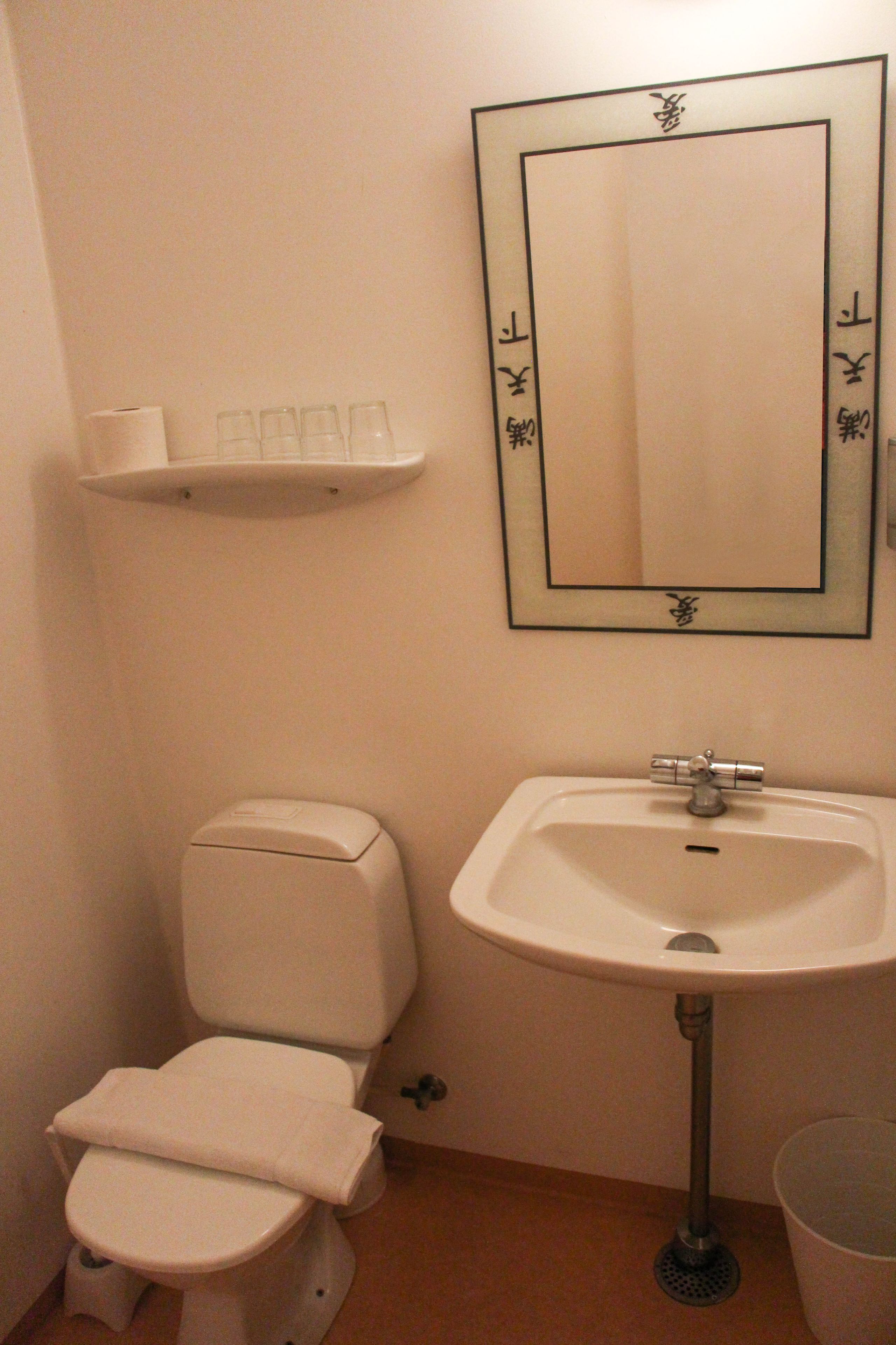 Un baño con inodoro, lavamanos y espejo con marco decorativo.