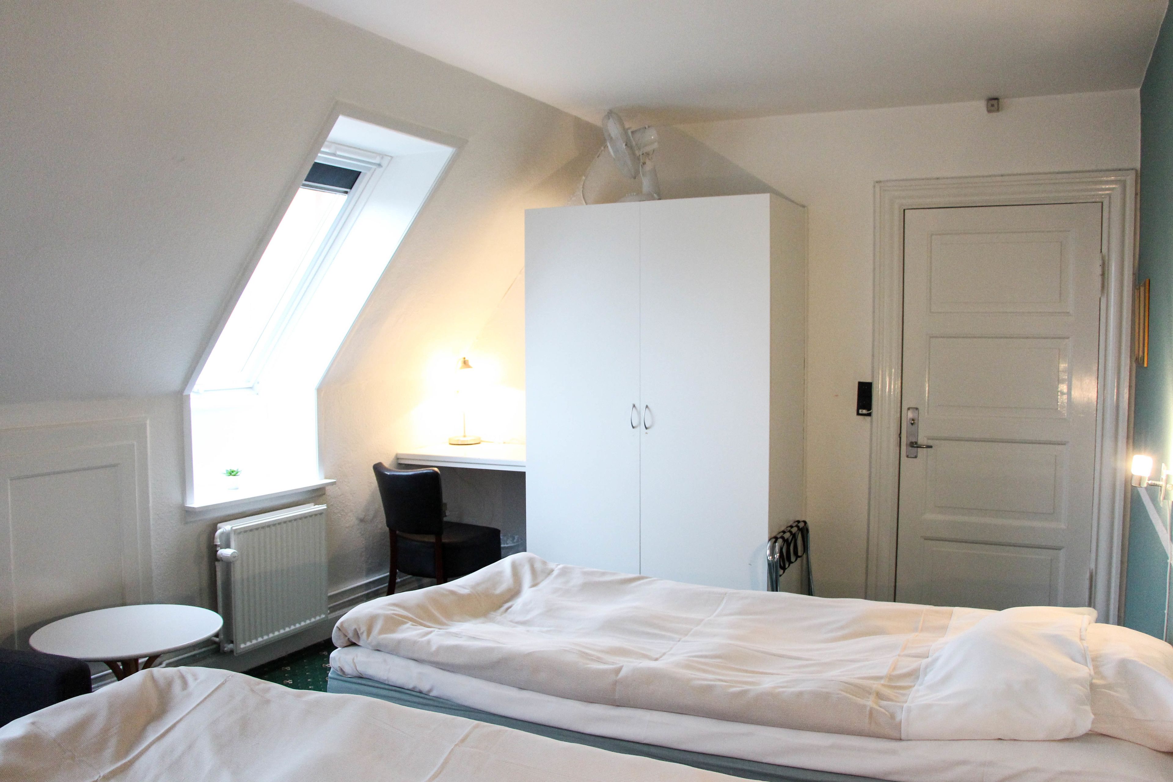 A room with two beds, a desk, a chair, and a radiator.