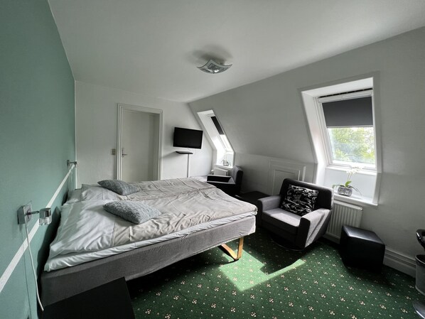 A bedroom with a bed, a chair, a TV, a window, and a radiator.