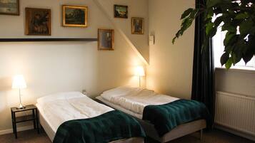 Ein Zimmer mit zwei Einzelbetten, einem kleinen Tisch, einer Lampe und einer Pflanze.