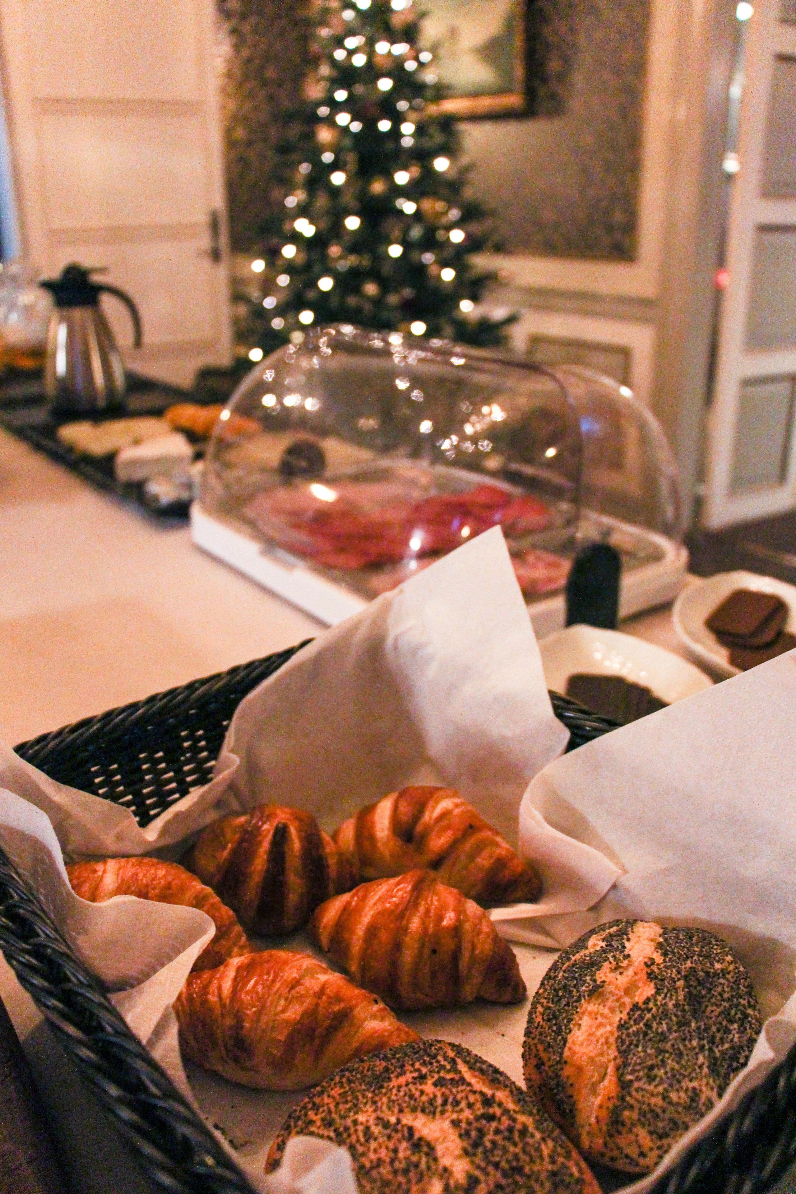 Un bufé de desayuno con cruasanes y otras bollerías, una estación de café y un árbol de Navidad al fondo.