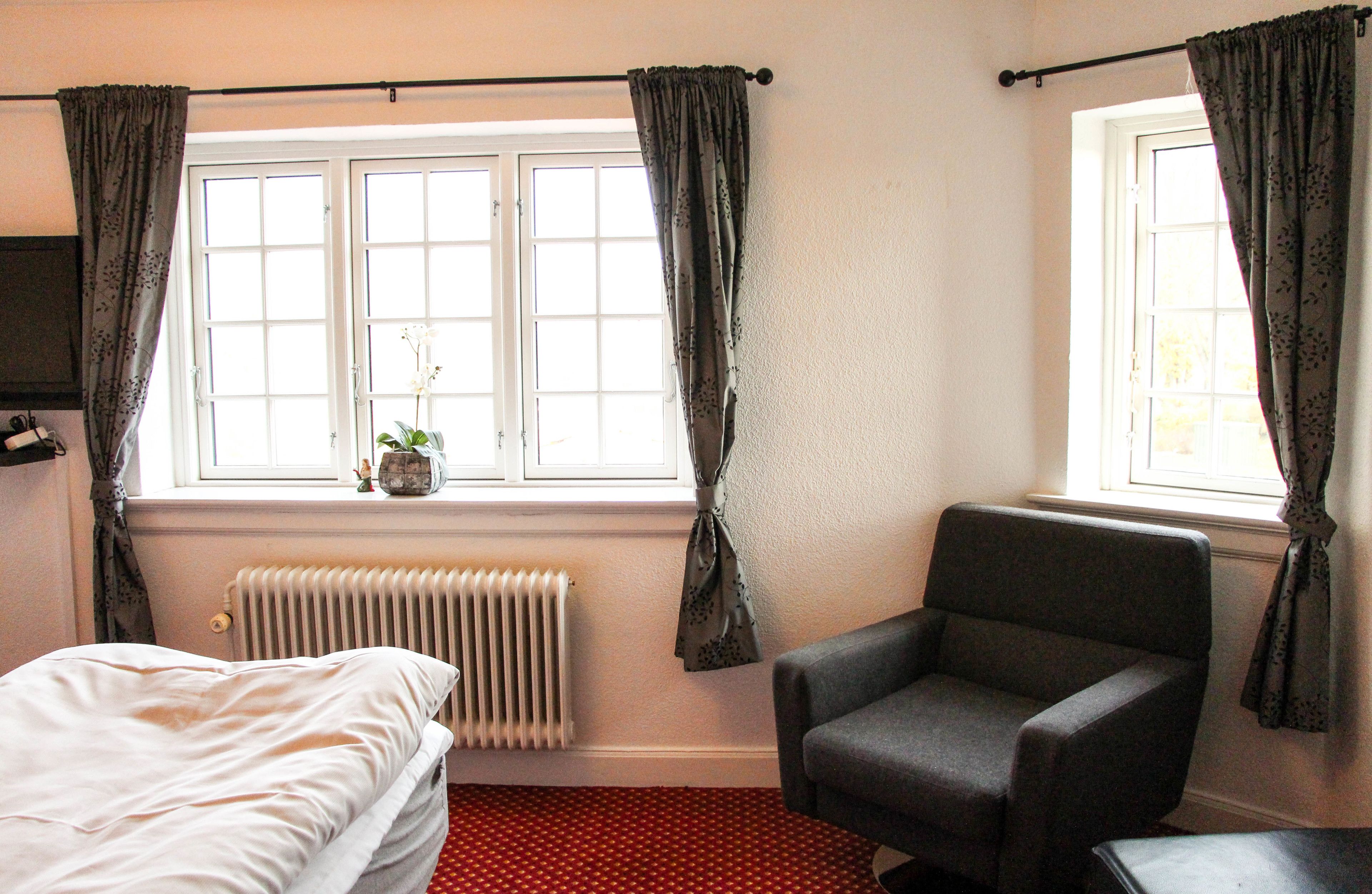 A bedroom with a bed, a chair, a radiator, and a window with curtains.