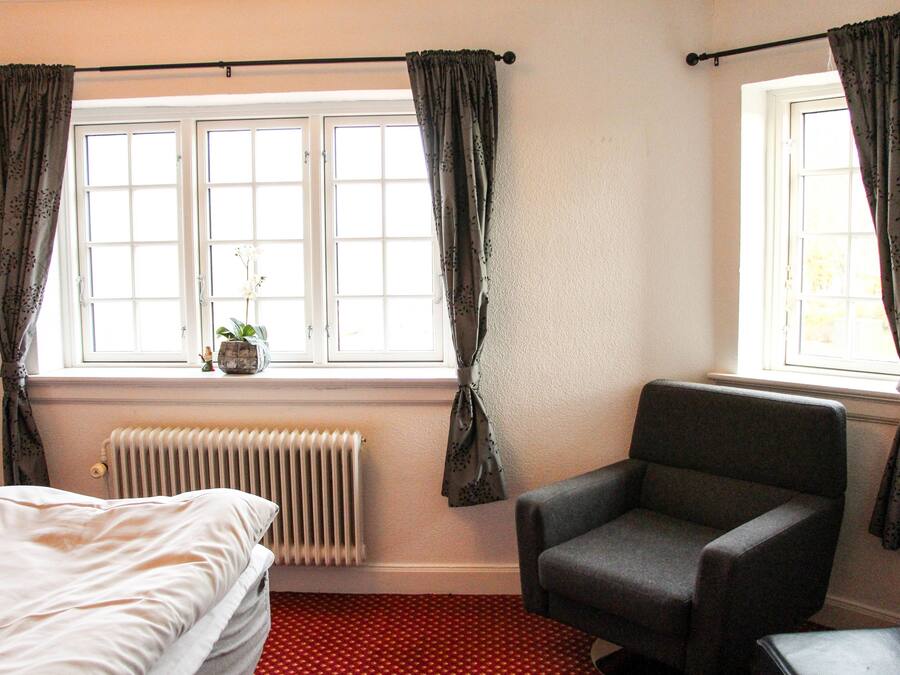 Un dormitorio con una cama, una silla, un radiador y una ventana con cortinas.
