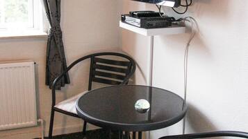 Una habitación pequeña con una televisión sobre un mueble bajo, una mesa redonda, dos sillas y un radiador.