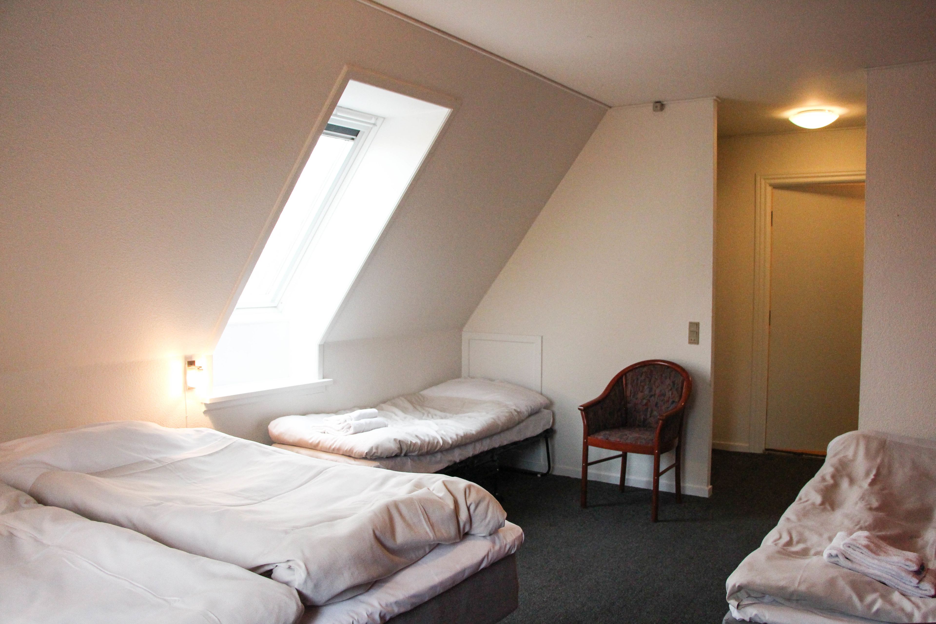 A small, dimly lit room with two beds, a chair, and a door.