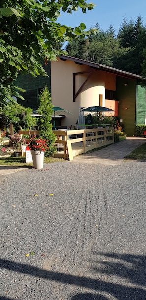 A building with a gravel driveway, a wooden fence, and a green umbrella. - Hôtel Le Pavillon (Cours)