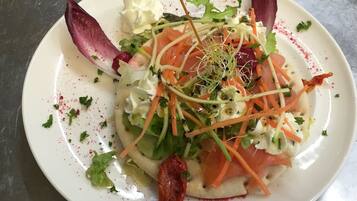A white plate with a salad, including greens, carrots, and a piece of meat, garnished with herbs and a toothpick.