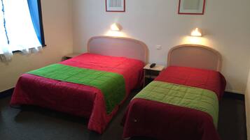 Dos camas individuales con colchas rojas y verdes, lámparas de noche y cuadros en la pared.