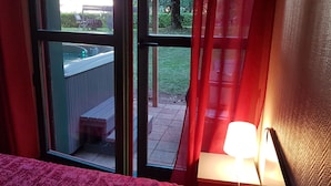 A room with a window overlooking a backyard, a wooden deck, and a hot tub. - Hôtel Le Pavillon (Cours)