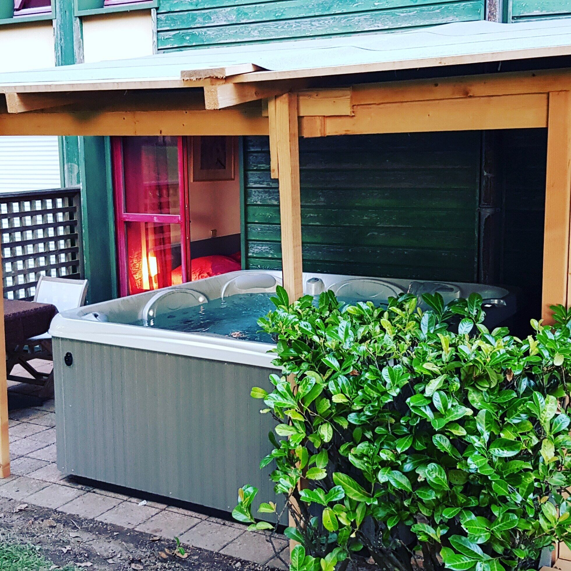 A hot tub under a wooden pergola, surrounded by greenery.