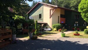A two-story building with a green and beige facade, a gravel driveway, and outdoor seating area with tables and chairs. - Hôtel Le Pavillon (Cours)