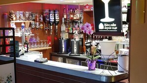 A bar area with a counter, shelves of bottles, and a sign above the counter. - Hôtel Le Pavillon (Cours)