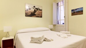 Une chambre d’hôtel comprenant un lit, une table de chevet, une fenêtre avec des rideaux et deux tableaux accrochés au mur.