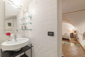 A modern bathroom with a white sink, glass shelves, and a mirrored wall.
