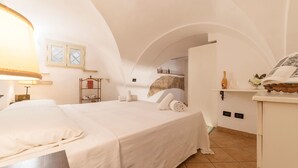 Quarto com cama grande, mesa de cabeceira, abajur, guarda-roupa e uma pequena janela.