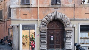 Um edifício com uma entrada em arco de pedra, uma vitrine com manequins e uma scooter estacionada.