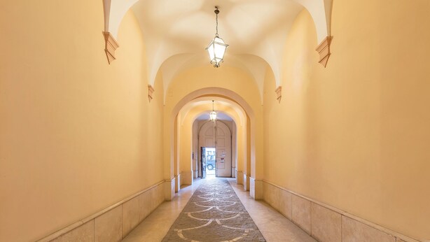 Um corredor longo e estreito com piso estampado, tetos em arco e luminárias pendentes.