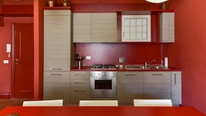 A compact kitchen with a red wall, stainless steel appliances, and a white countertop. - Navona Charming Apartment (Rome)